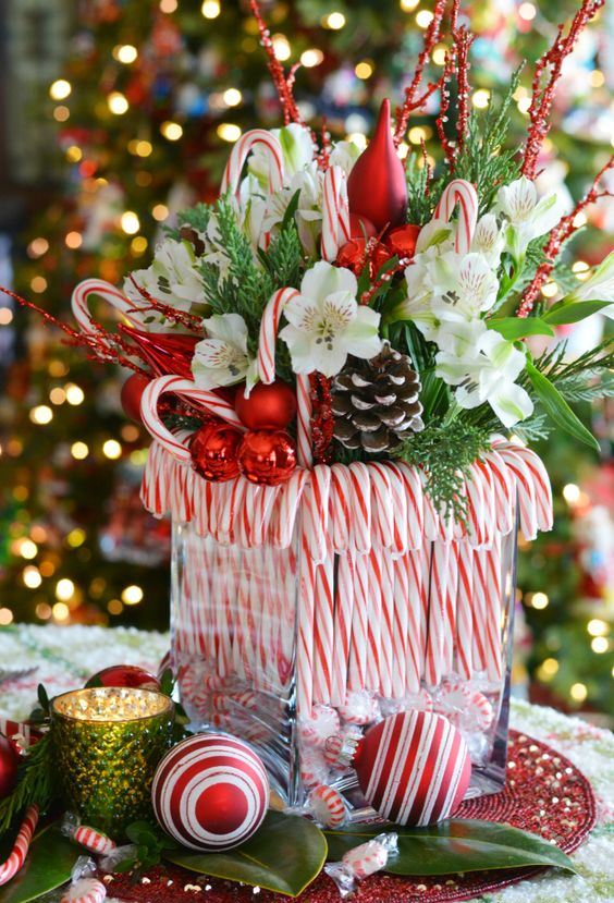 a bright Christmas centerpiece of a vase with candy canes, greenery, white blooms, snowy pinecones, candy canes and branches