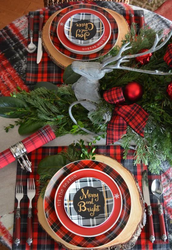 a bright Christmas tablescape with red plaid linens, chargers, ribbon, evergreens and red Christmas ornaments is cheerful