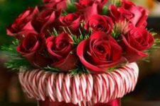 a bright holiday centerpiece -a vase wrapped with candy canes and with greenery and red roses is a very refined and chic idea