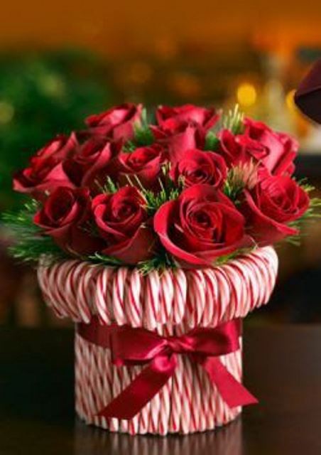 a bright holiday centerpiece -a vase wrapped with candy canes and with greenery and red roses is a very refined and chic idea