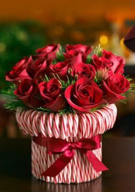 a bright holiday centerpiece -a vase wrapped with candy canes and with greenery and red roses is a very refined and chic idea