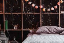 a catchy bedorom with a shelving unit covered with string lights and an additional string light garland, a bed with mauve bedding and candle lanterns