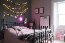 a catchy grey and pink bedroom with a black metal bed, string lights with photos, artwork and a crystal chandelier