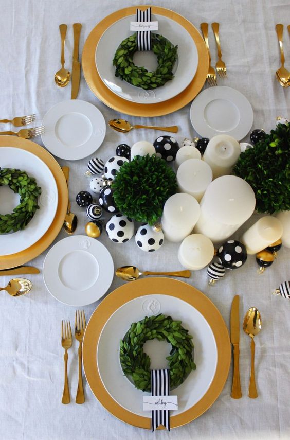 a chic and glam Christmas tablescape with black and white polka dot ornaments, pillar candles and greenery wreaths plus gold cutlery and chargers