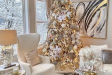 a chic and refined Christmas tree with white fabric blooms, white and gold glitter ornaments, gold glitter ribbons and icy branches on top