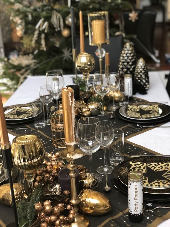 a chic black and gold NYE party tablescape with black table runners and placemats, black and gold plates, gold candles and candleholders