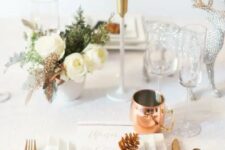 a chic holiday tablescape with white blooms, copper cutlery and mugs and a silver deer figurine for a sparkly touch