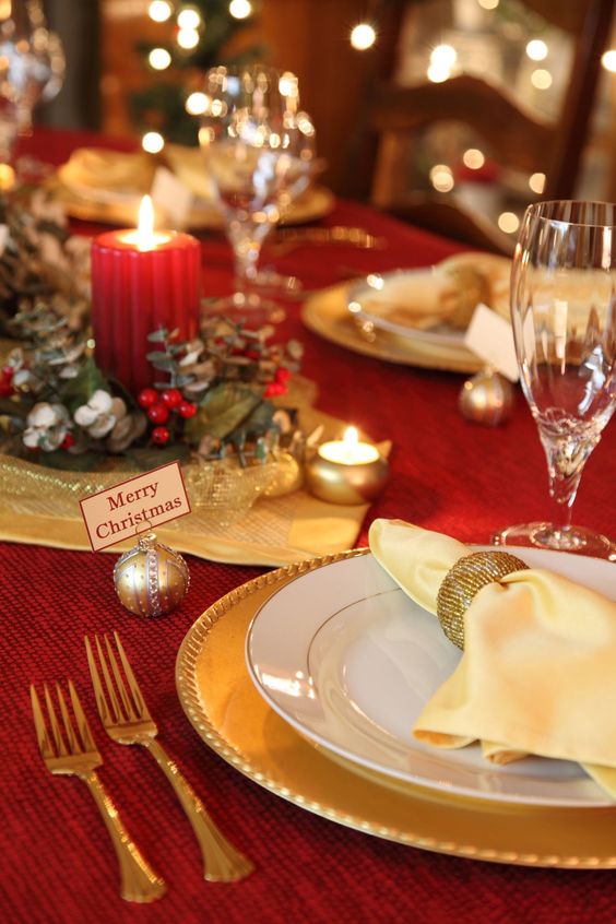 a chic red and gold Christmas table with a greenery and candle centerpiece, gold chargers and cutlery, mini candles and ornaments