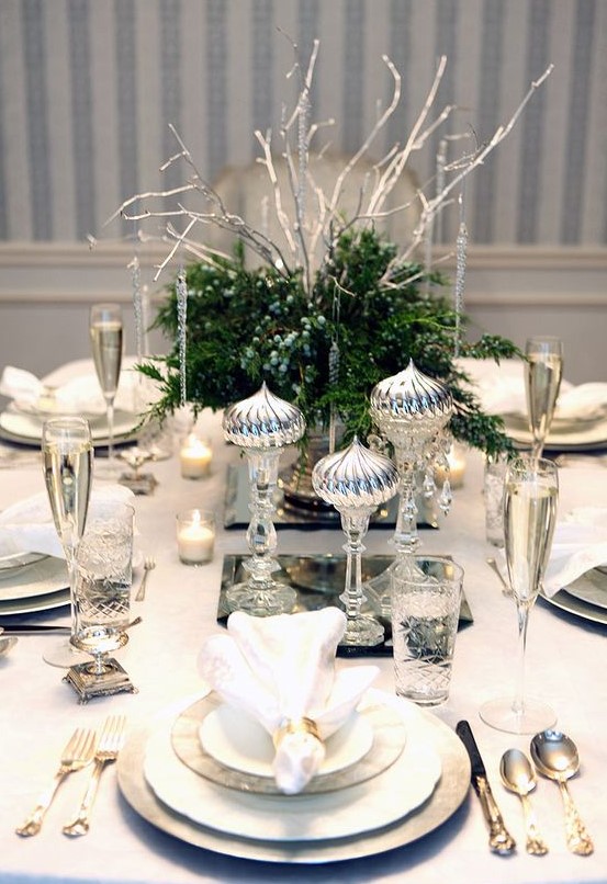 a chic silver-infused table setting with greenery and berries and silver imitating icicles and silver cutlery and chargers