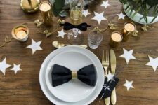 a chic table setting with white and gold stars, white blooms, eucalyptus, gold cutlery and candle holders