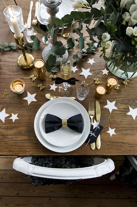 a chic table setting with white and gold stars, white blooms, eucalyptus, gold cutlery and candle holders