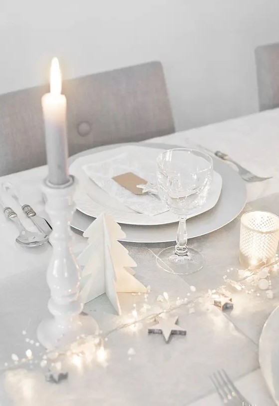 a clean white tablescape with a dove grey table runner, LEDs, stars, candles and wooden fir trees