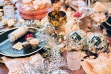 a colorful tablescape with disco balls, tinsel and gold cutlery for a sparkly New Year party