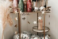 a cool NYE bar cart with ombre bottles, pampas grass and colored grasses, silver disco balls and a star garland
