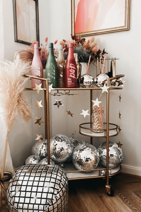 a cool NYE bar cart with ombre bottles, pampas grass and colored grasses, silver disco balls and a star garland