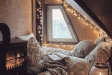 a cpzy attic sleeping space with a bed on the floor, lots of pillows, string lights all over the space and a hearth with lights