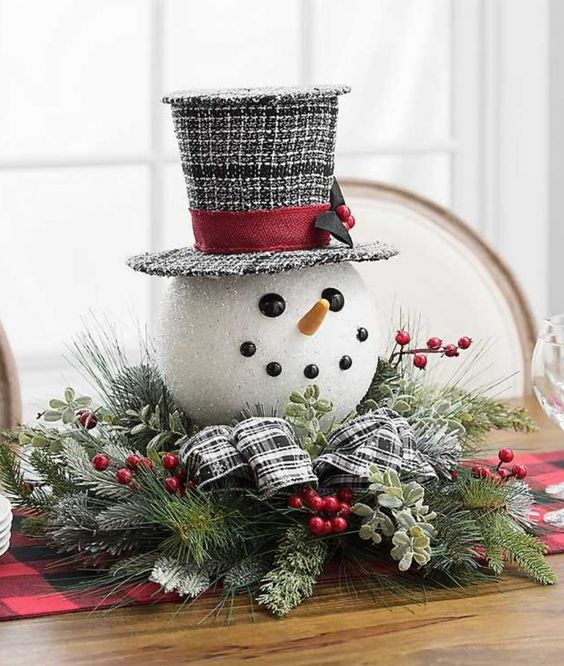 a cute Christmas centerpiece of faux evergreens, greenery, berries, a snowman head in a top hat is a fun and cool idea
