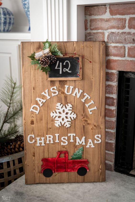 a cute Christmas sign of a wooden plaque with white letters, a red turck, evergreens, pinecones and a chalkboard house number