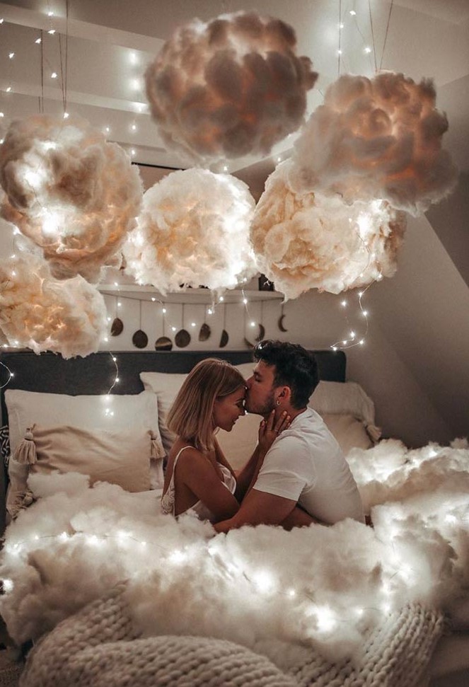 a fantastic 'on cloud 9' bedroom with a black bed with neutral bedding, a fluffy blanket, clouds over the bed, string lights over the bed and on it