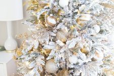 a flocked Christmas tree with gold and white printed and solid ornaments, gold branches, white snowflakes is chic