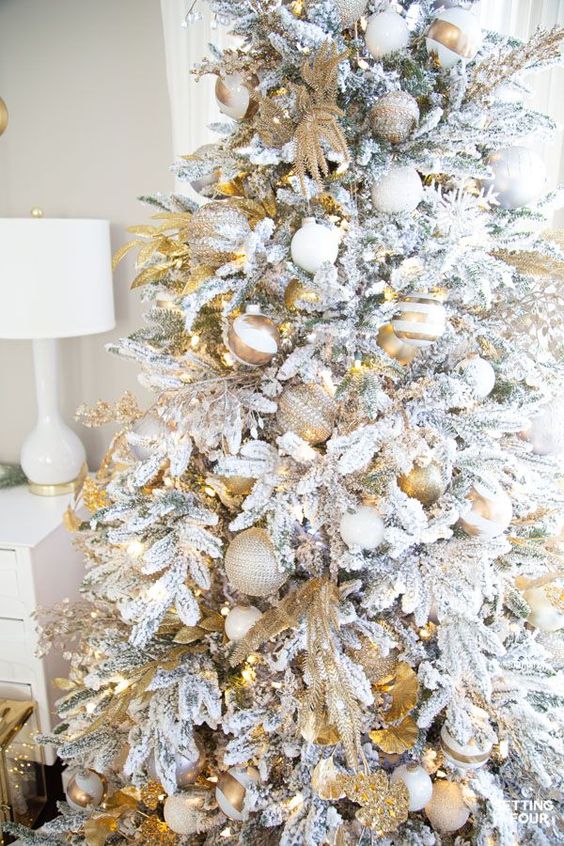 a flocked Christmas tree with gold and white printed and solid ornaments, gold branches, white snowflakes is chic