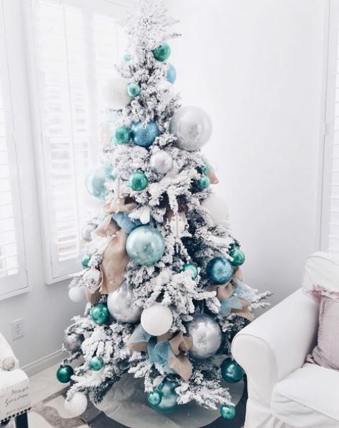 a flocked Christmas tree with green, blue and silver ornaments of various sizes for a lovely and very modern look