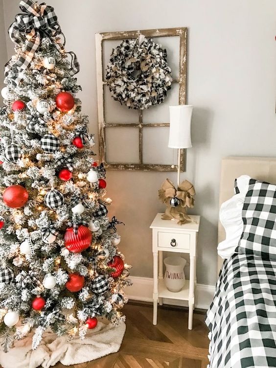 a flocked Christmas tree with oversized red, buffalo check ornaments, an oversized bow on top and some lights is wow