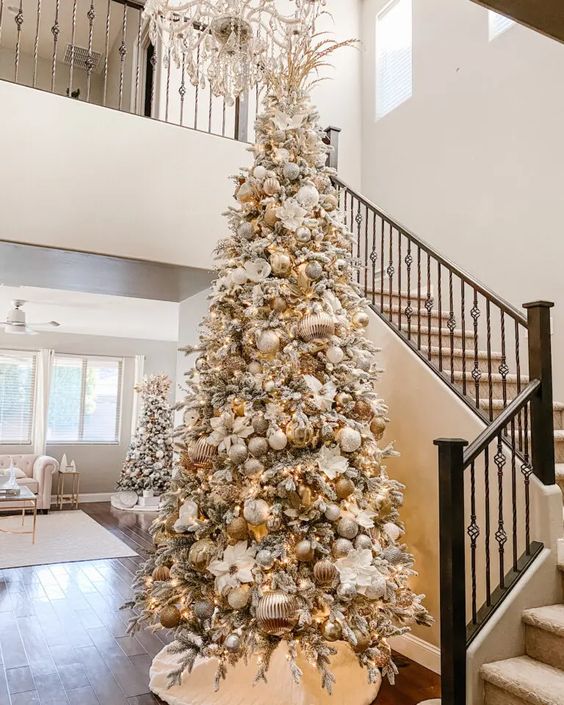 a flocked Christmas tree with white, silver and gold ornaments, white faux blooms and gold leaves and branches on top