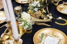 a gorgeous black and gold table setting with candles, antlers, gold chargers, white blooms and greenery
