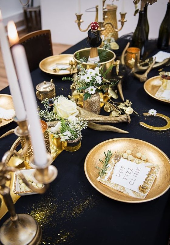 a gorgeous black and gold table setting with candles, antlers, gold chargers, white blooms and greenery