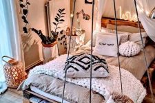 a gorgeous boho bedroom with a pallet bed with neutral bedding and blankets, nightstands with table lamps, a pendant chait, star-shaped string lights over the bed