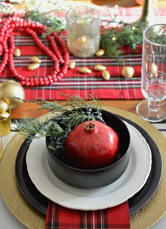 a gorgeous plaid Christmas tablescape with plaid linens, gold nuts and ornaments, red beads and a pomegranate in a bowl