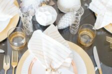 a grey and gold table setting with cone Christmas trees, geometric ornaments, gilded cutlery and glasses