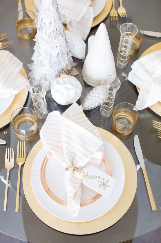 a grey and gold table setting with cone Christmas trees, geometric ornaments, gilded cutlery and glasses