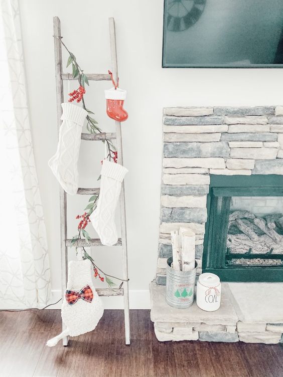 a ladder with evergreens and red berries, white stockings and a red Christmas ornament for holiday styling