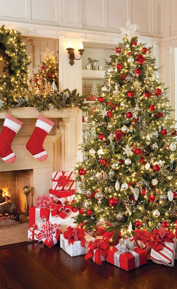 a large Christmas tree with red, gold and mother of pearl ornaments, lights and lots of red and white gift boxes
