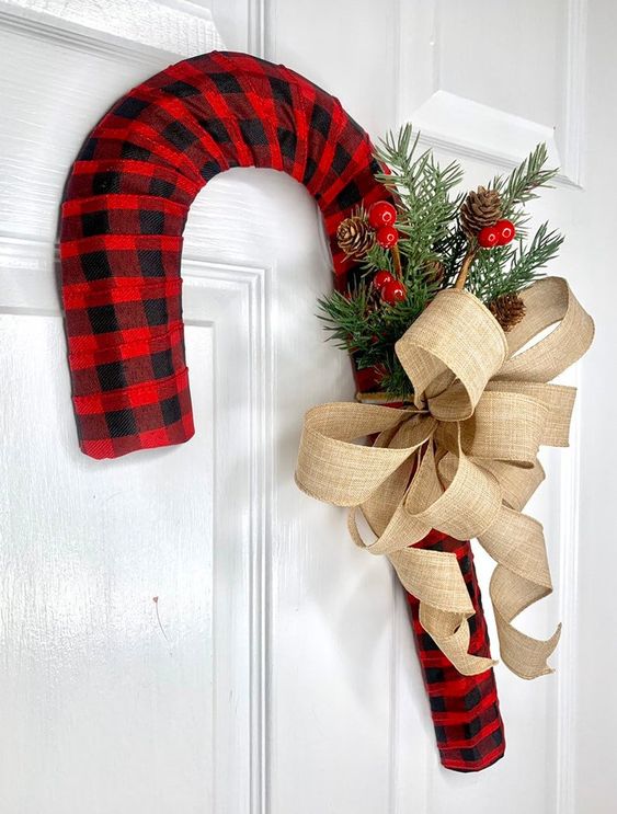 a large bright plaid candy cane wreath with a burlap bow, fir branches, berries and pinecones is a lovely idea for outdoors