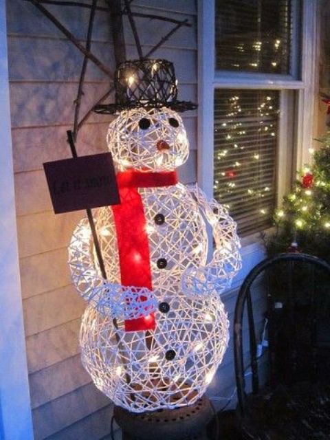 a lit up yarn snowman with a red scarf and a black top hat is a creative outdoor decoration for Christmas