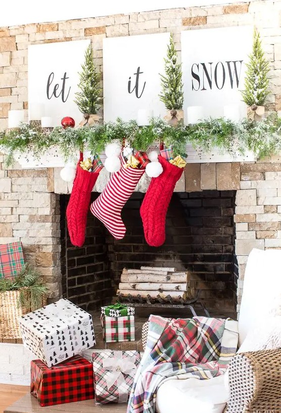 a lovely Christmas mantel with a snowy evergreen garland, red sotckings, ornaments, candles, tree and signs is a very bold and cool idea