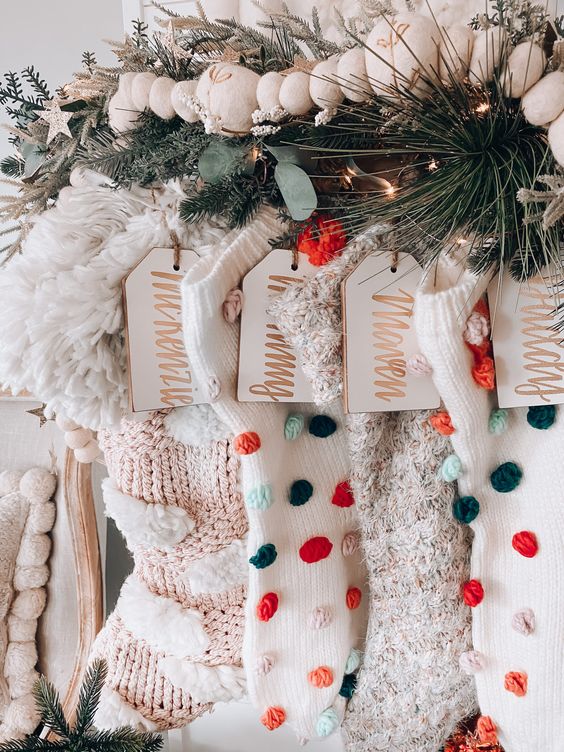 a lovely Christmas mantel with neutral stockings with pompoms and fringe, wooden tags, an evergreen garland and wooden beads