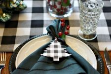 a lovely Christmas tablescape with a buffalo check runner and napkin tags, berries and a pillar candle in a jar and elegant glasses