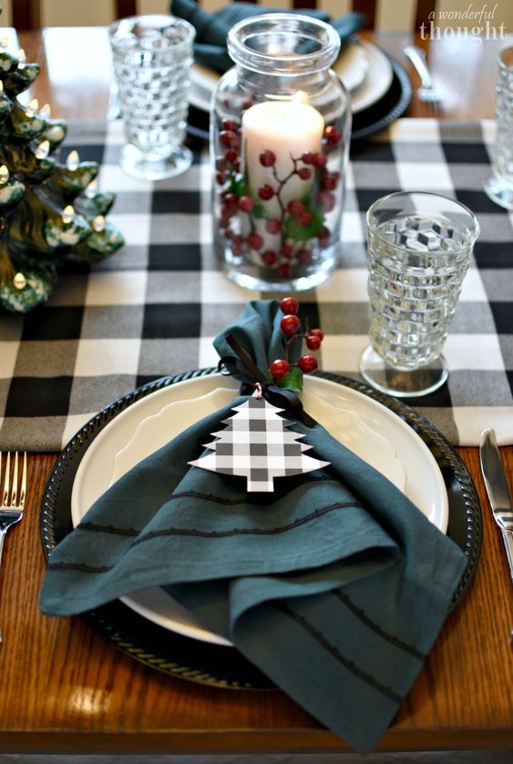 a lovely Christmas tablescape with a buffalo check runner and napkin tags, berries and a pillar candle in a jar and elegant glasses