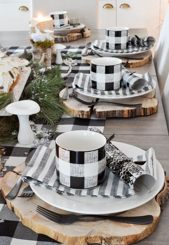 a lovely rustic Christmas table setting with buffalo check mugs and a runner, wood slice placemats, evergreens and candles