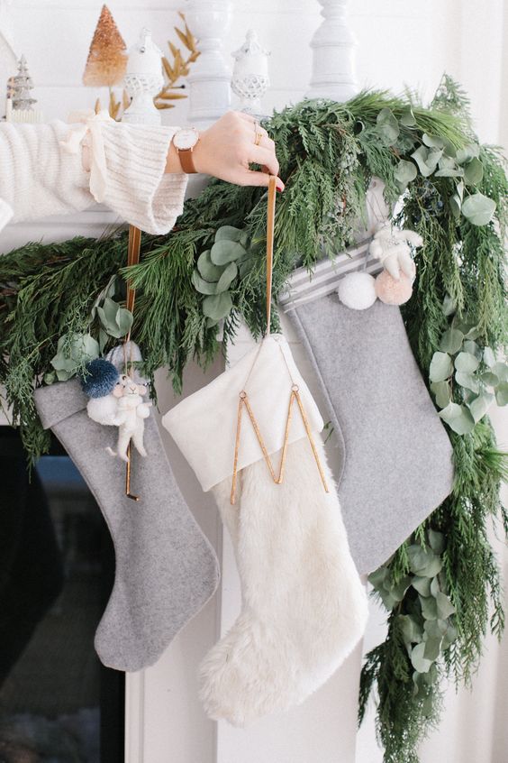 a modern Christmas mantel with a lush greenery and evergreen garland, white and grey felt stockings, pompoms is a very cool idea