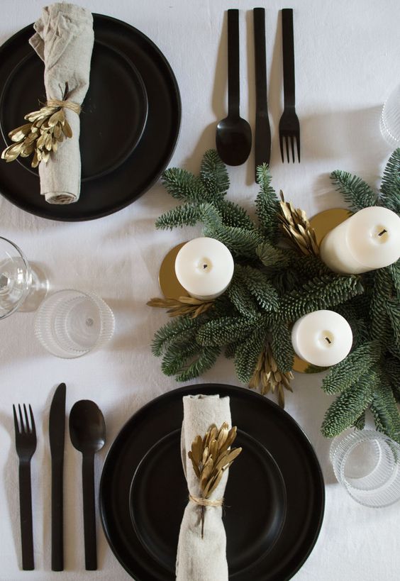 a modern and stylish Christmas tablescape with black plates and chargers, black cutlery, gold foliage and candleholders and fir branches