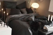 a moody bedroom with taupe walls, a dark bed with black bedding, a white dresser, a black leather bench and a branch covered with fairy lights