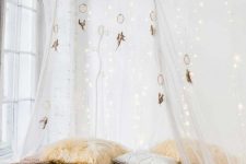 a neutral bedroom with a low bed right on the floor, pastel bedding, a semi sheer canopy with lights and dream catchers over the bed
