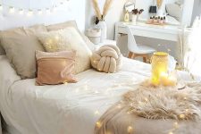 a neutral boho bedroom with a white bed with string lights, a sleek vanity with a mirror, macrame and fringe hangings