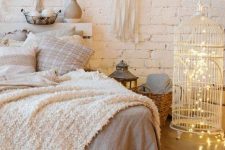 a neutral boho bedroom with a white planked bed and neutral bedding, a cage with lights inside as a light source, some fringe and boho hangings