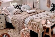 a neutral boho bedroom with layered bedding, a shelf gallery wall, a canopy with lights, candle lanterns and a rattan chair